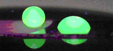 The image shows two water drops illuminated with a fluorescent dye. The drop on the left (the one that looks round) is sitting on a nanowire surface with a very hydrophobic coating. The drop on the right, which is spread out, is sitting on a flat surface with the same coating.