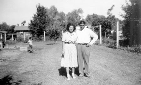 A black and white photo of a man and woman posing on a dirt path in a rural setting.