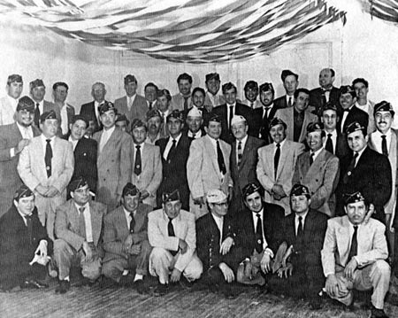 A group of men in suits and military caps posed for a formal group photograph, with streamers on the ceiling.