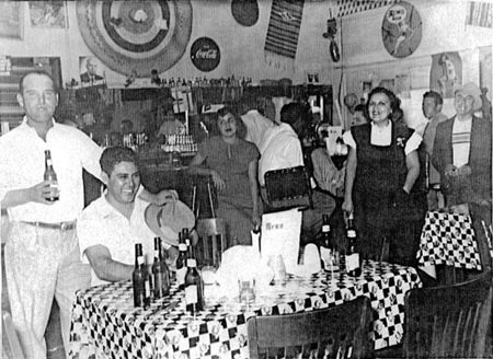 A black-and-white photo of people in a restaurant with checkered tablecloths and drink bottles.