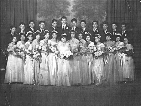 A vintage black-and-white group photo of young women in gowns and young men in suits at a formal event.