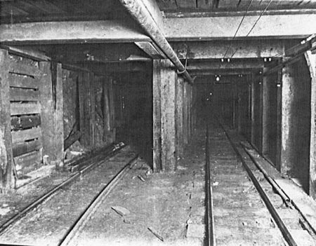 Underground mine tunnel with wooden beams and narrow gauge tracks.