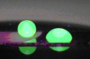 The image shows two water drops illuminated with a fluorescent dye. The drop on the left (the one that looks round) is sitting on a nanowire surface with a very hydrophobic coating. The drop on the right, which is spread out, is sitting on a flat surface with the same coating. This picture shows that the nanowires create a lotus leaf-like surface. Arizona State University researchers have made that surface photoresponsive and can make the drop on the left move in response to light.