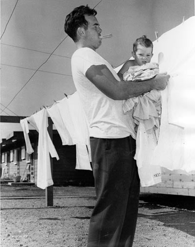 Student hanging laundry with a child in his arms  
in 'Victory Village,' 1949-50