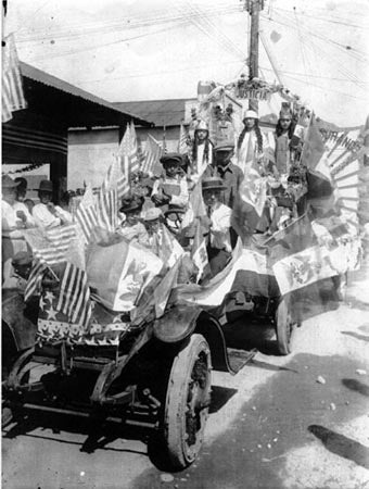 Black-and-white photo of a decorated parade float with flags and participants, featuring the word Justicia.