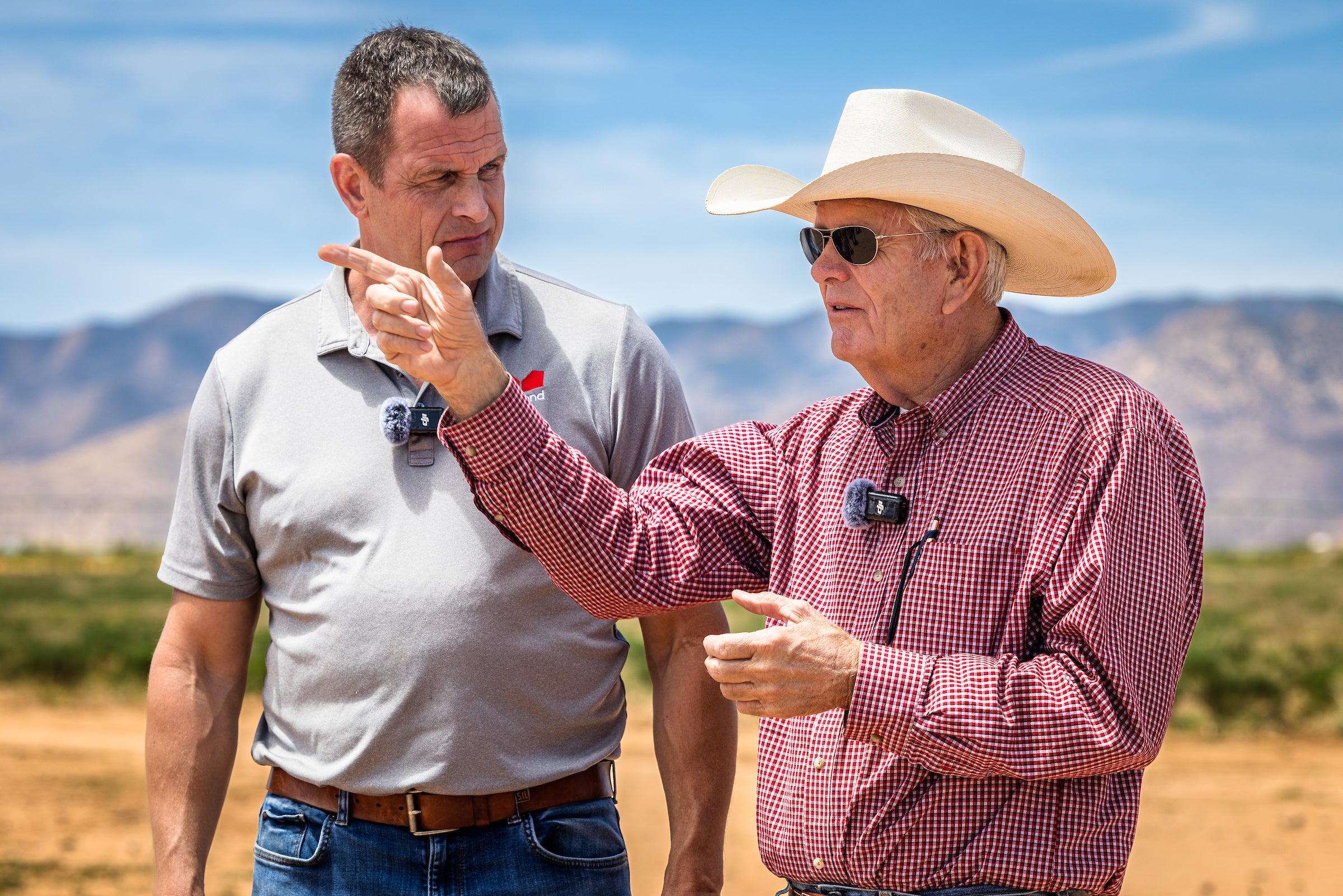 Two men conversing outdoors with mountain range behind them