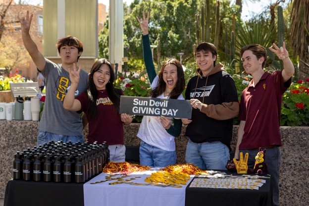 Five students standing at a table holding a Sun Devil Giving Day sign