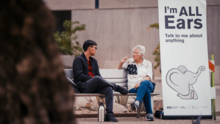 Older woman speaking to younger man on a bench.